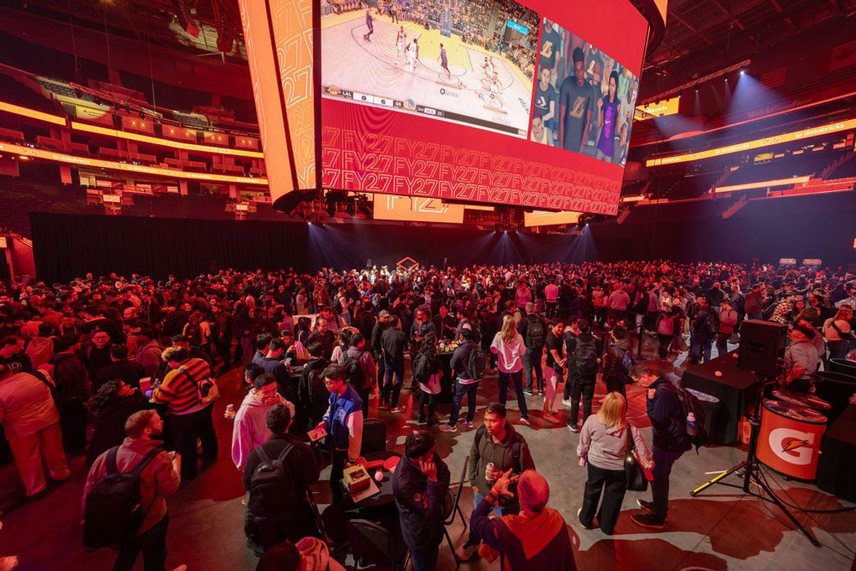 Large crowd of attendees networking in arena venue with red lighting and large screens overhead