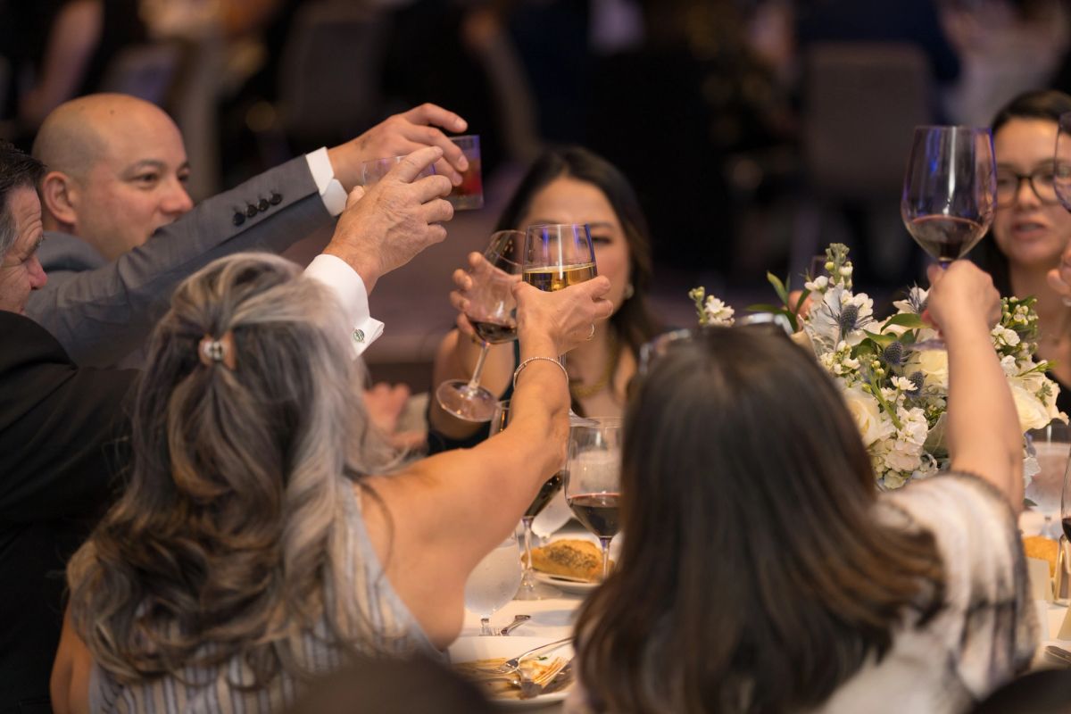 Gala attendees raise wine glasses in a toast at formal dinner event with floral centerpieces