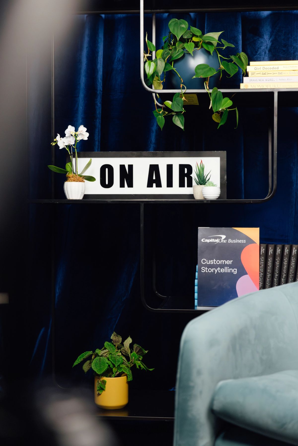 Cozy office corner with "ON AIR" sign, plants, and Customer Storytelling book on dark blue shelving unit