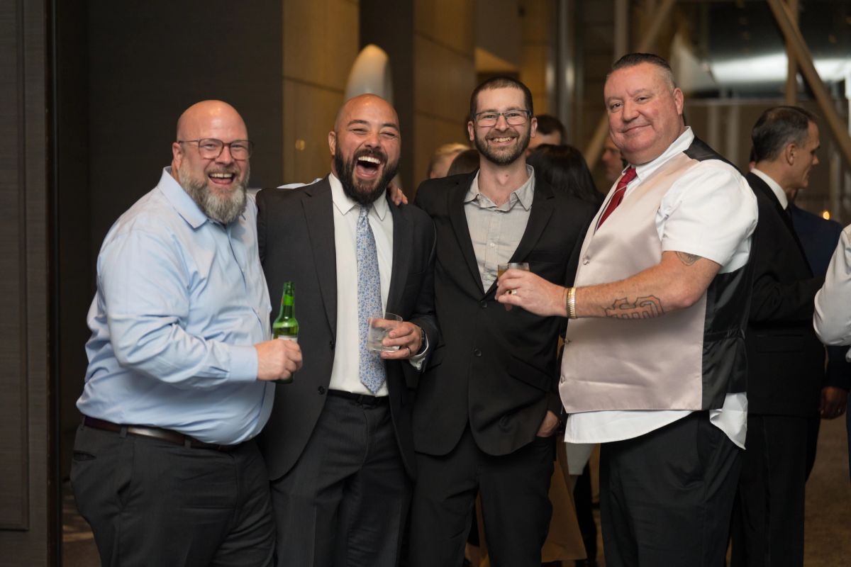 Four men in business attire smiling and posing together at an indoor networking event