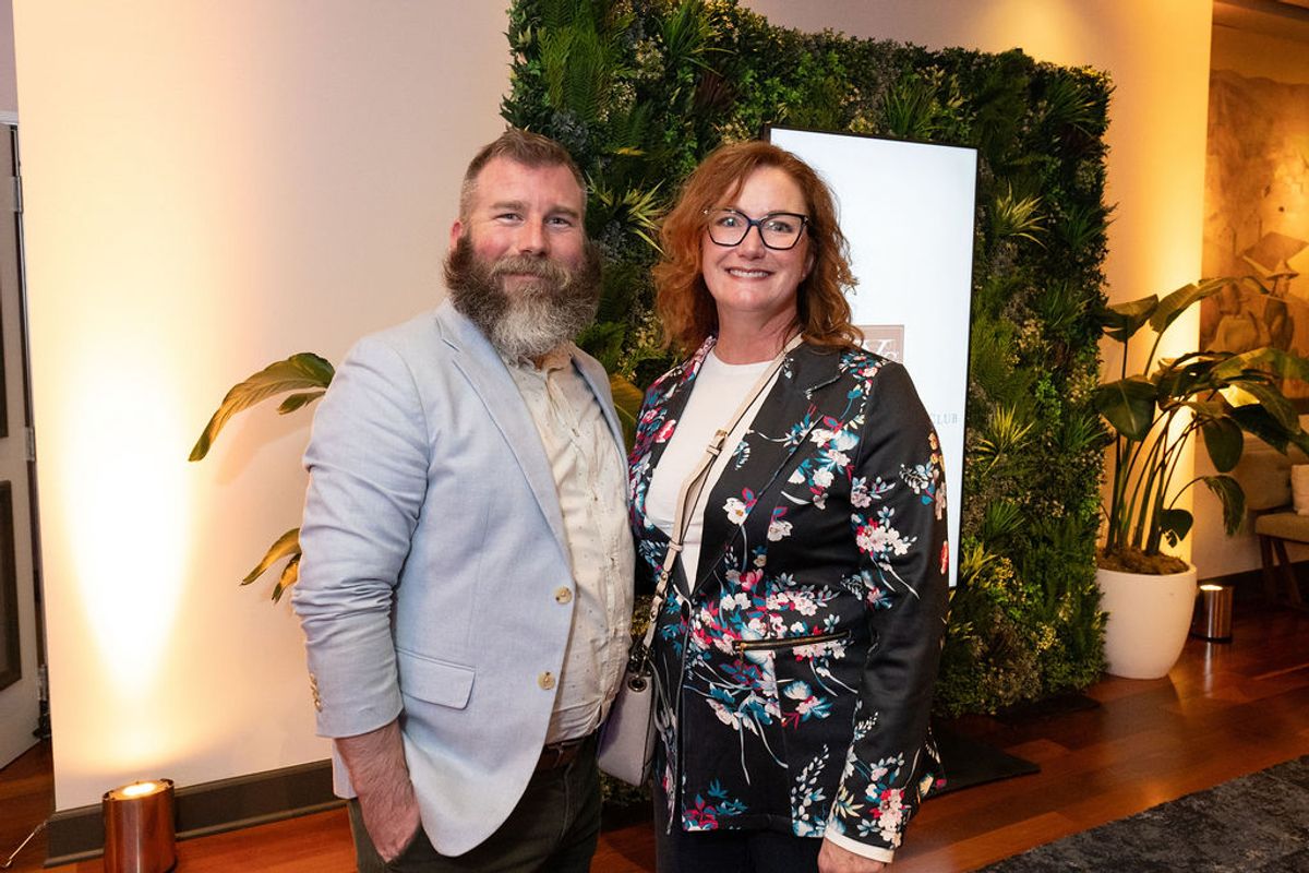 Two people networking at an indoor reception, standing by a green plant wall with warm lighting