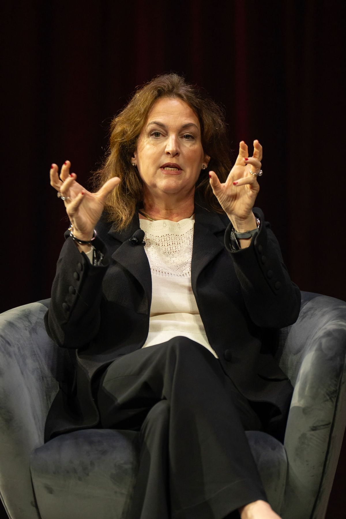 Speaker gesturing with both hands while seated in blue chair during conference presentation