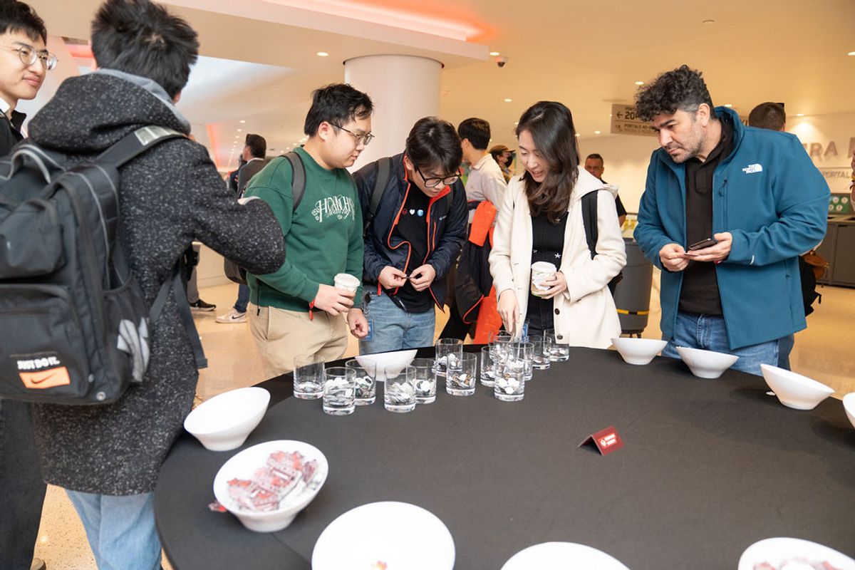 Attendees gather around a table with glasses and plates at an indoor conference event