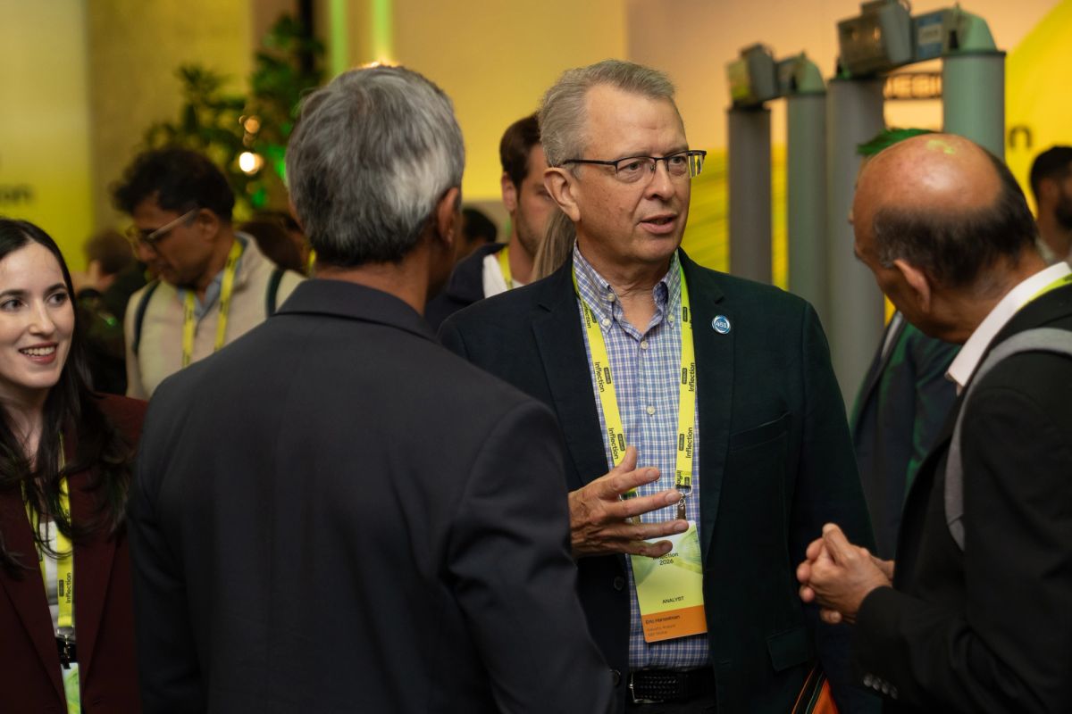 Attendees networking at a conference, with a man in a blazer gesturing while speaking to others.