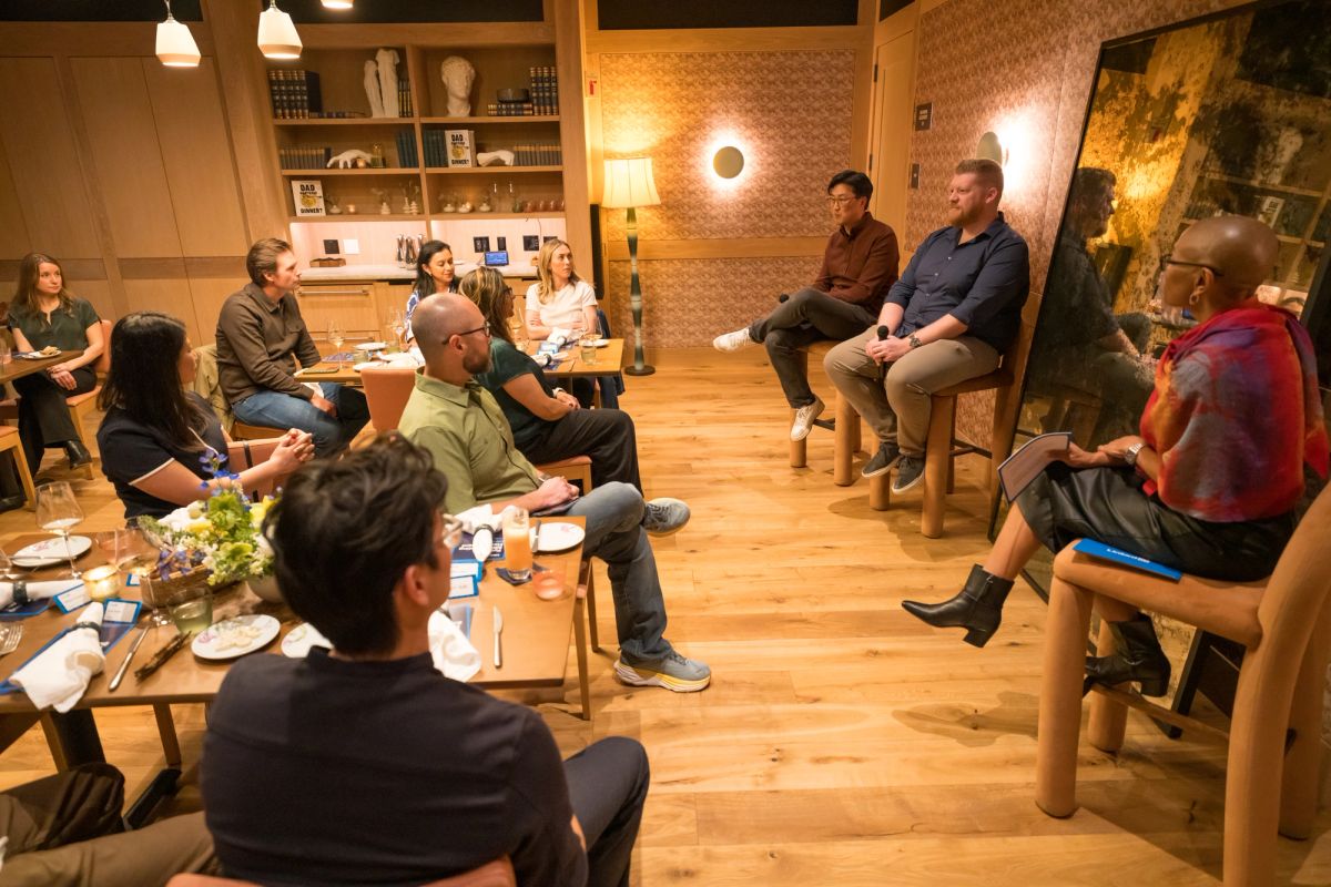 Panel discussion with speakers seated on stage and audience members sitting in chairs in a warm, wood-paneled.
