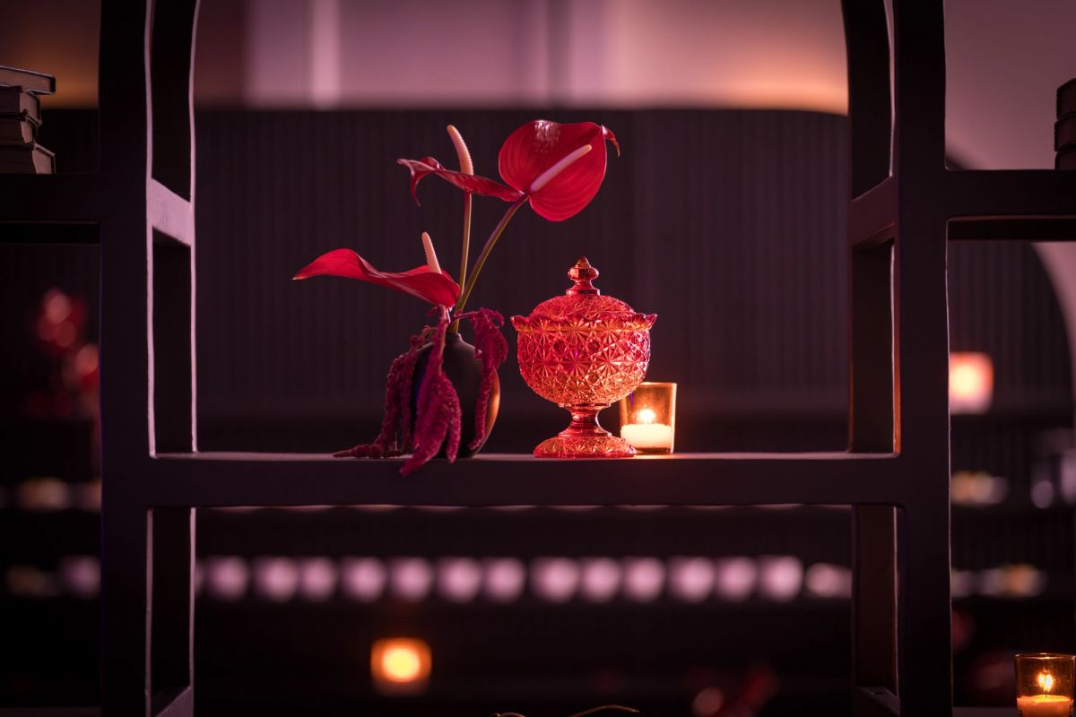 Decorative plant with red leaves in ornate glass bowl on dark shelf with warm ambient lighting