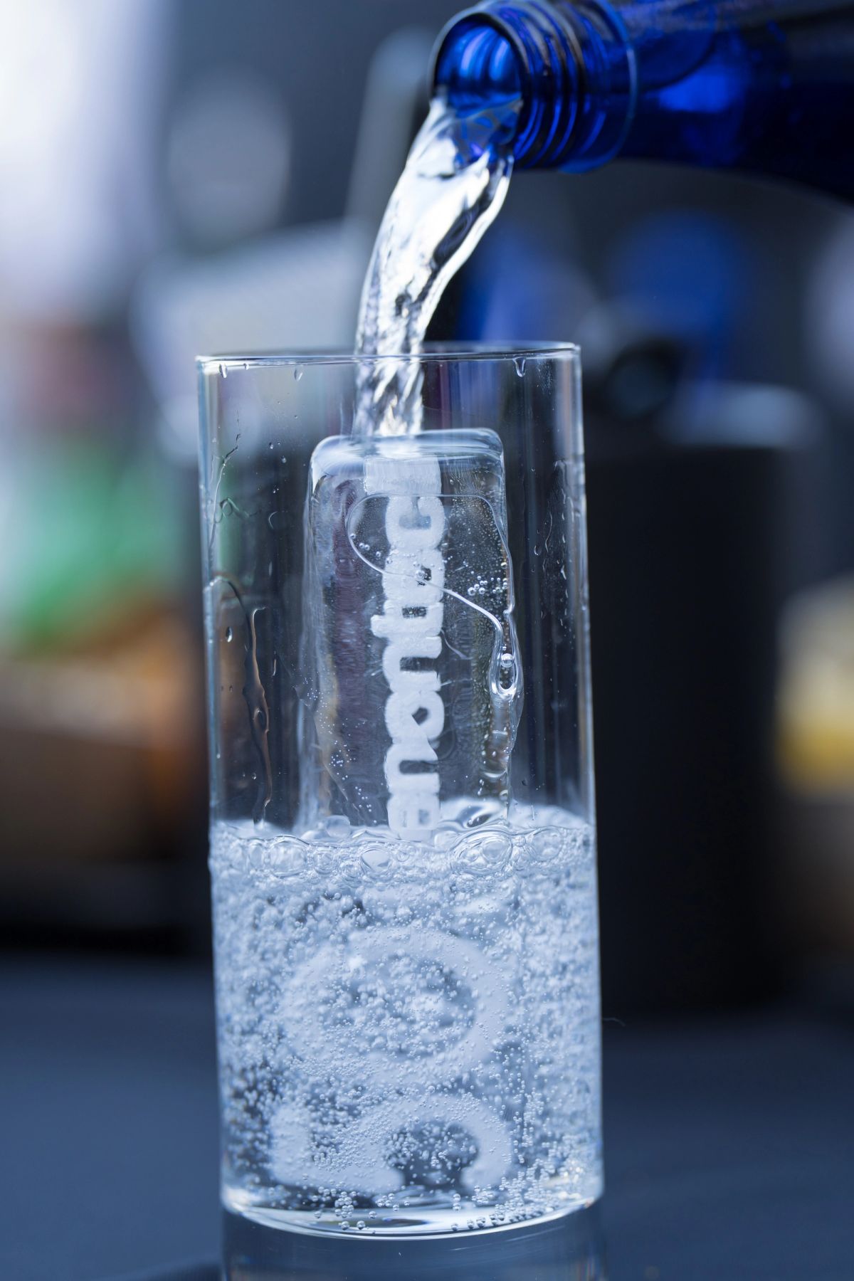 Water being poured from a blue bottle into a clear glass with bubbles, creating a refreshing drink.