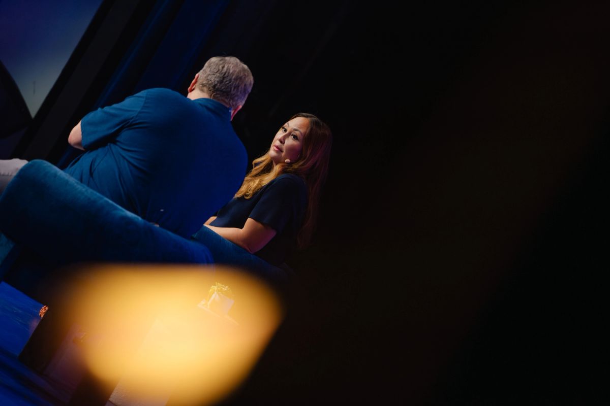 Two people sitting and talking in a dimly lit theater setting with warm stage lighting