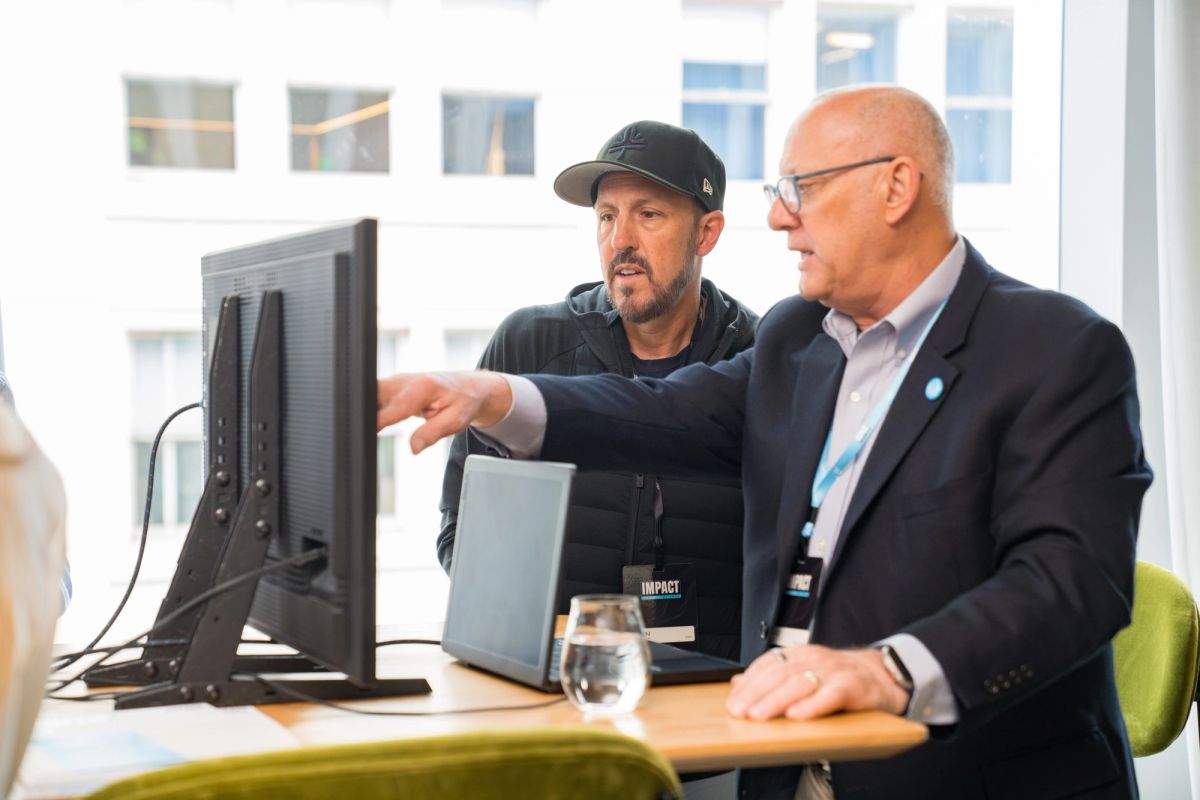 Two men collaborate at a computer workstation, one pointing at the monitor while the other observes during a.