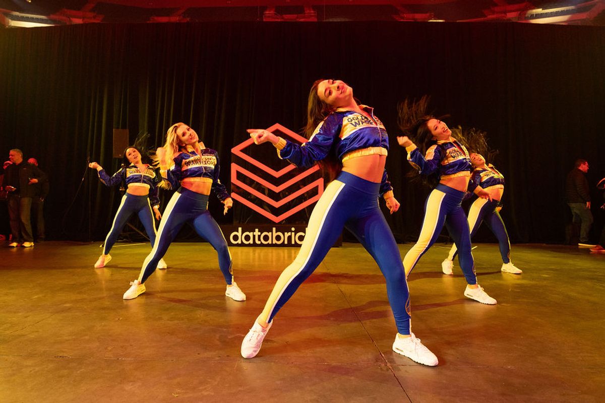 Dance performers in blue uniforms on stage with Databricks logo backdrop at conference venue