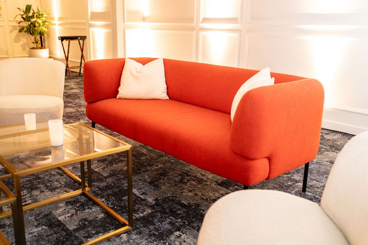 Modern orange sofa with white pillow in bright lounge area with glass coffee table and area rug
