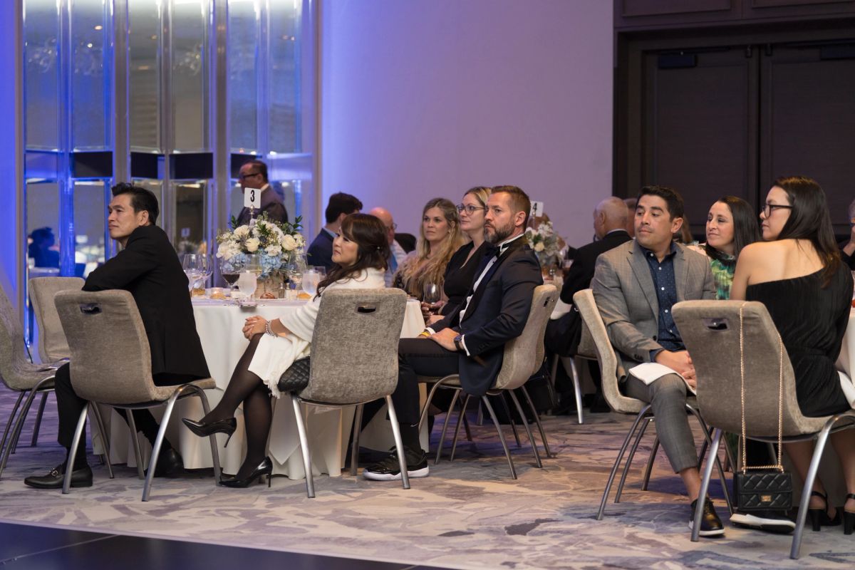 Formally dressed attendees seated at tables with white floral centerpieces during an elegant evening event