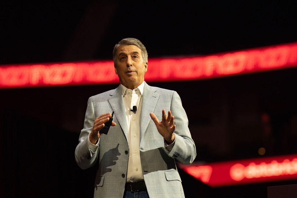 Executive in light gray suit presenting on stage with red lighting in background at conference venue