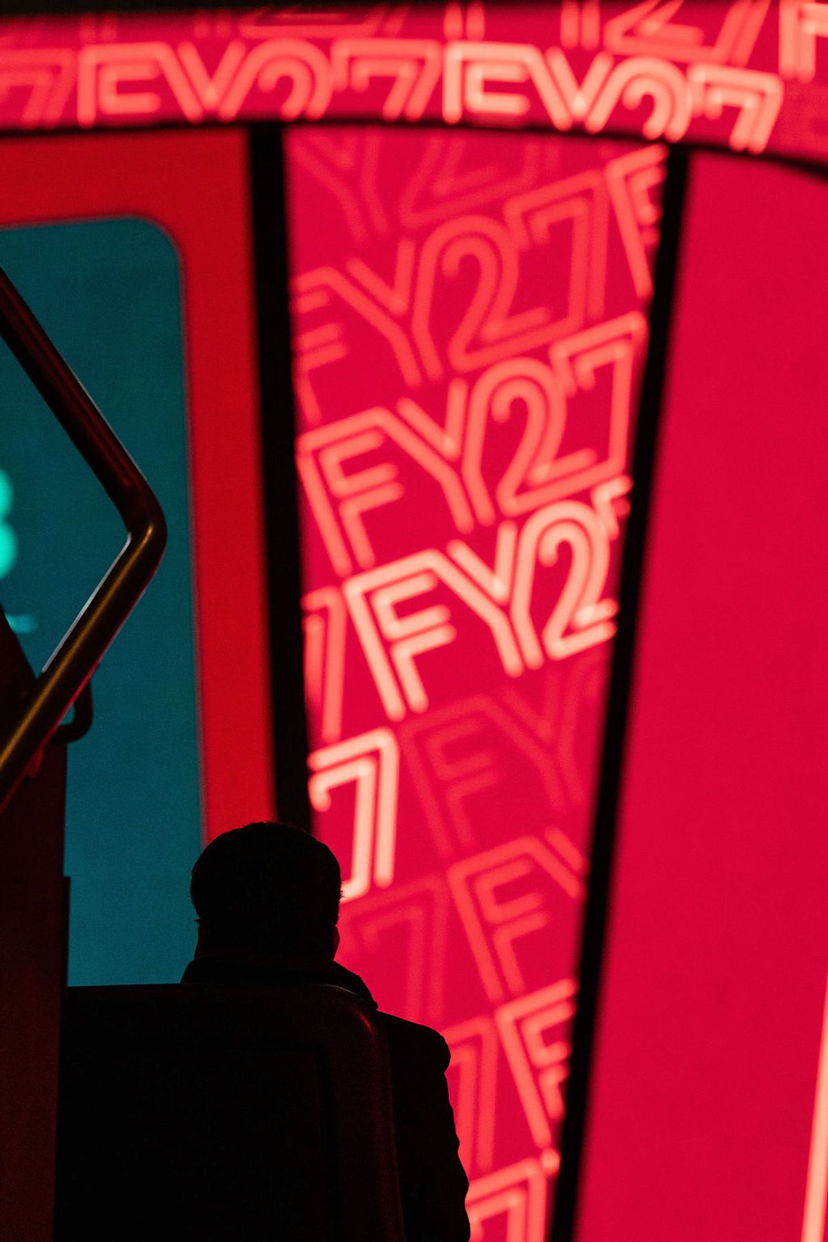 Silhouette of person against red backdrop with repeated "FY27" text at conference venue