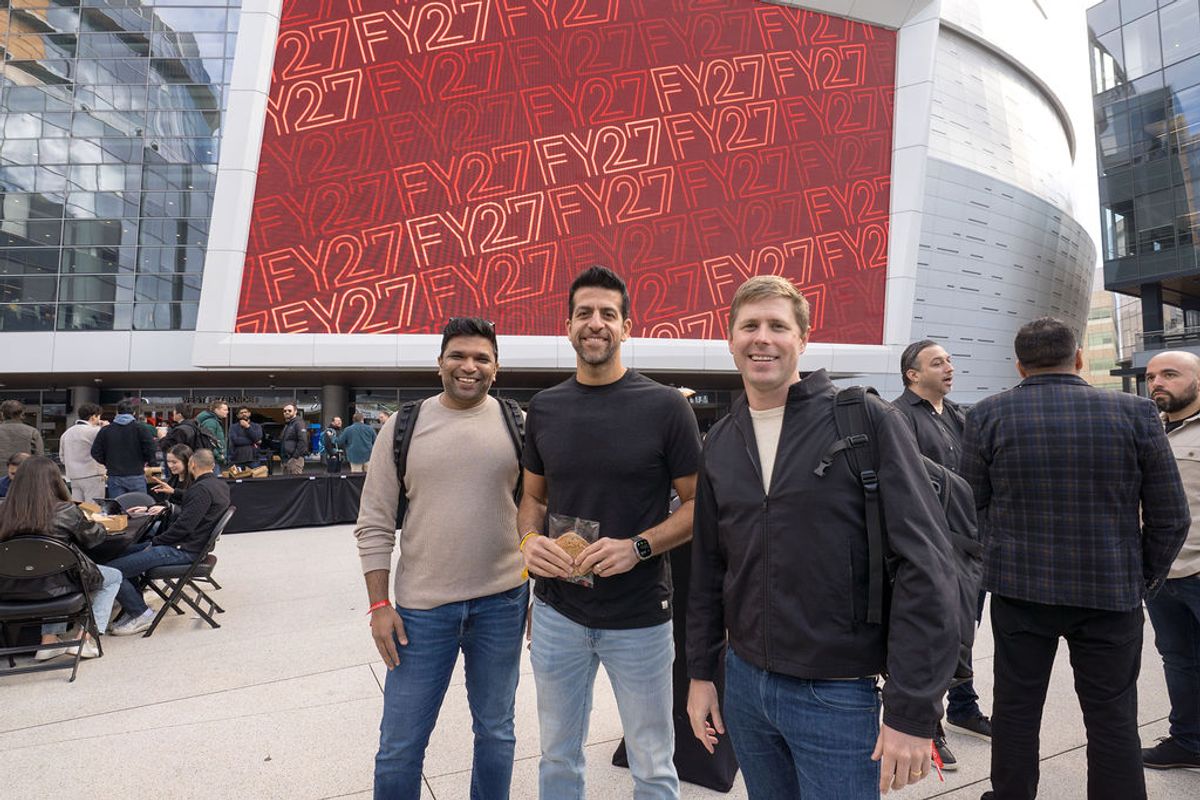 Three men pose together at a tech conference with F27 branding displayed on a large screen behind them
