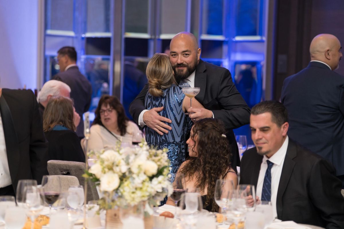 Attendees networking and embracing at an elegant evening gala with formal dining tables and city views