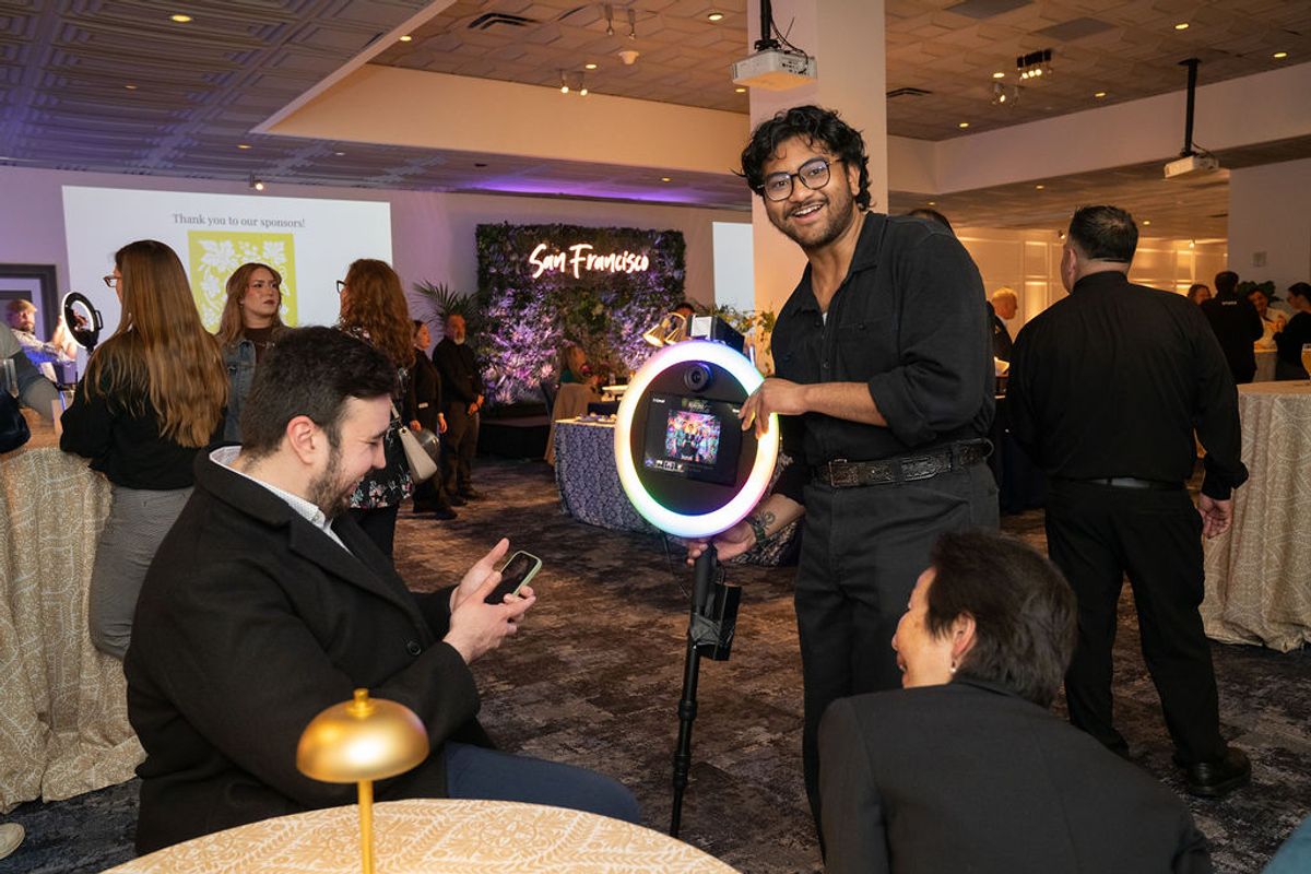 Attendees at networking reception with ring light photo setup, one person posing while another uses phone