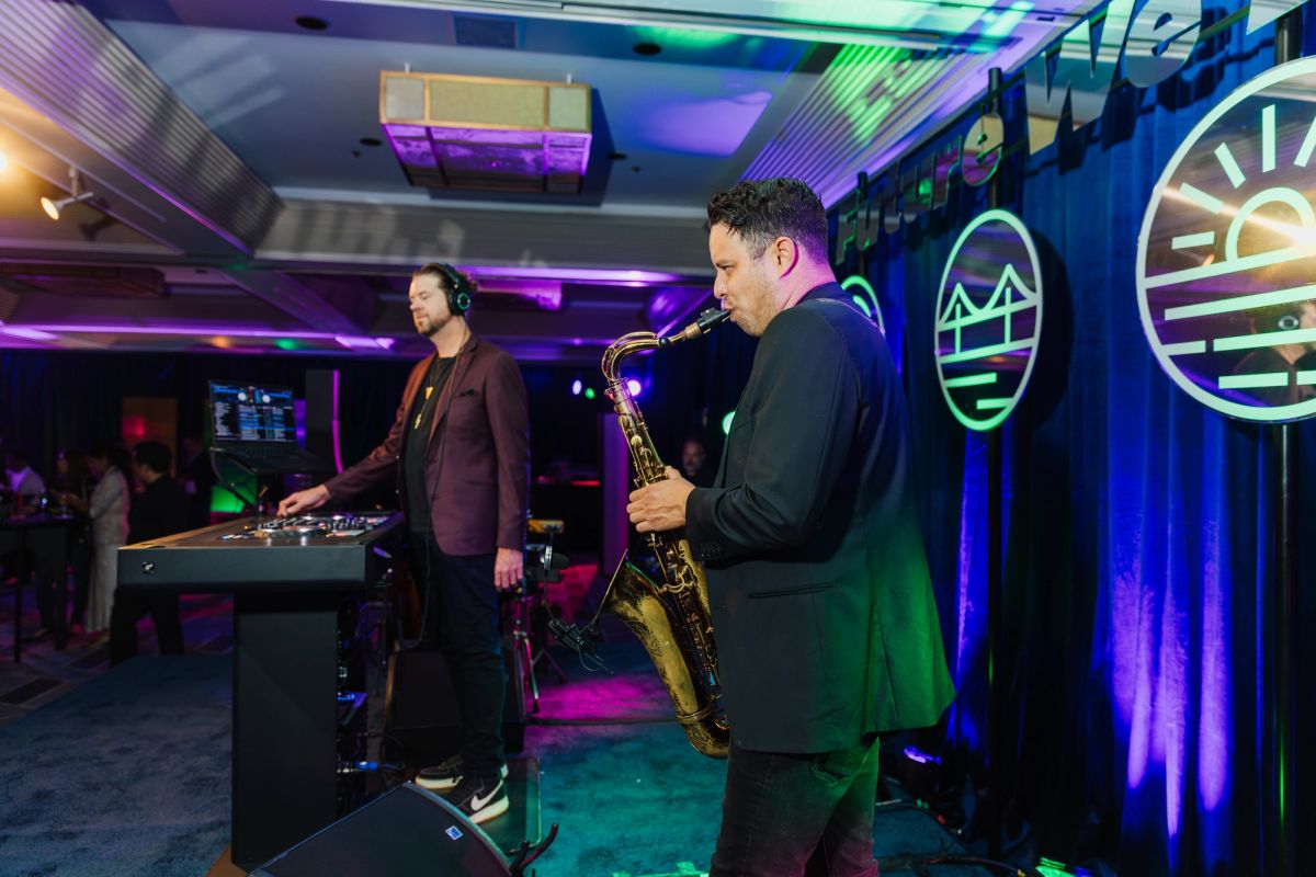DJ and saxophone player performing on stage with colorful lighting and circular logos on backdrop