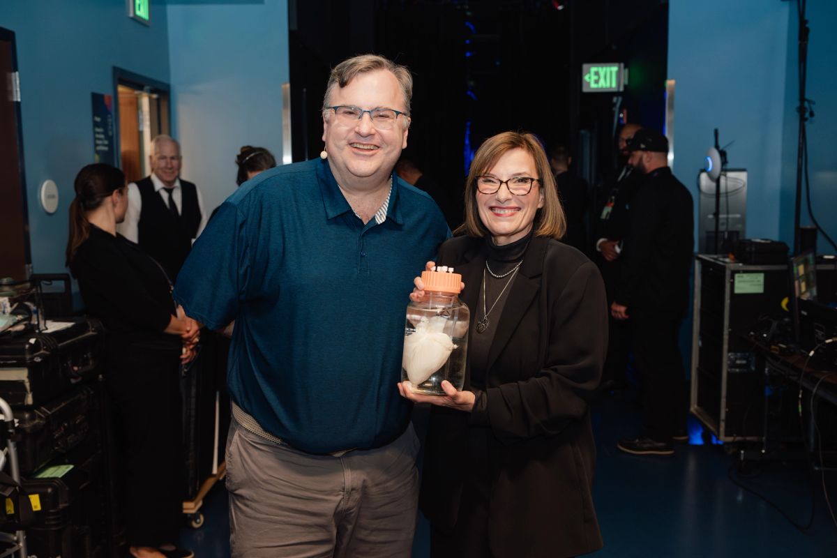 Two people posing together at an indoor event, one holding a glass jar award or gift item