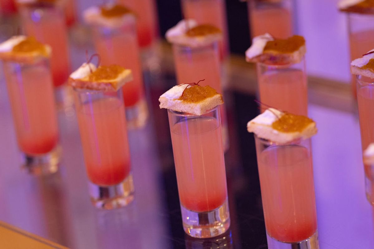 Multiple pink cocktails with orange garnishes arranged on a reflective surface at a networking reception