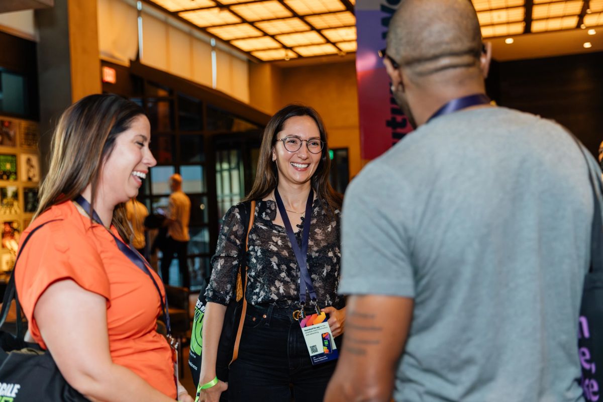Three people networking and laughing at a conference, with warm lighting and modern venue interior.