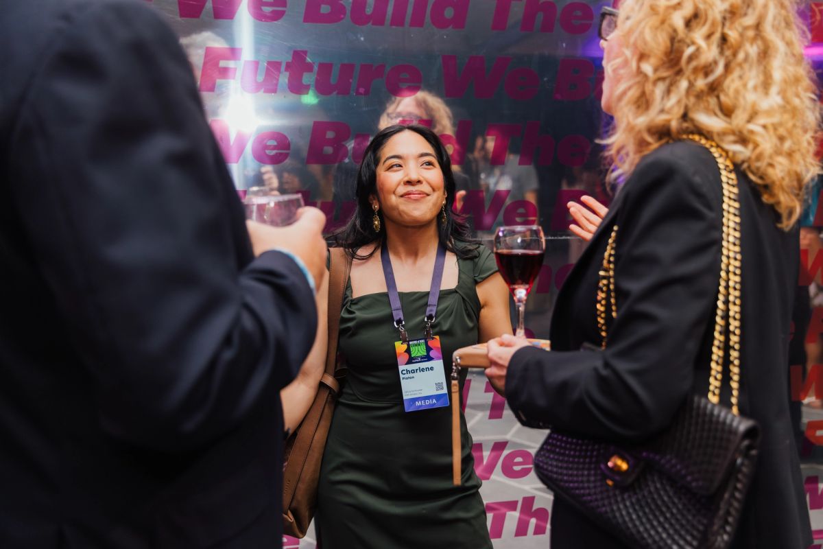 Three attendees networking at a conference, with one woman in green dress smiling while holding wine glass