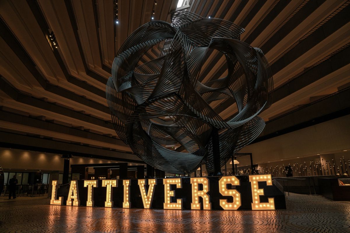 Lattiverse marquee letters glow before a large metal sphere sculpture in a hotel lobby.