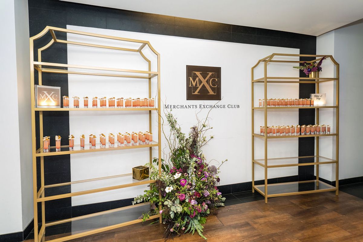 Gold shelving displays with bottles at Merchants Exchange Club networking reception, with floral arrangement