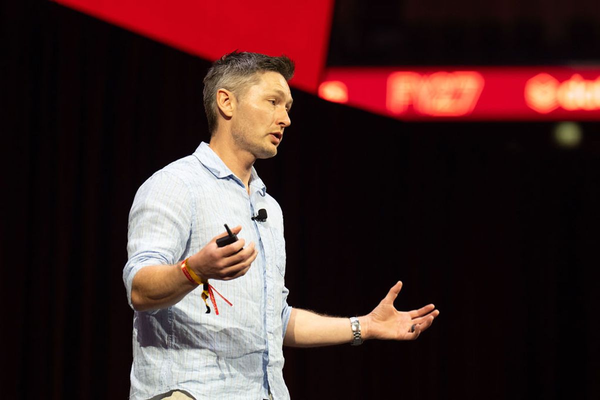 Speaker presenting on stage with microphone and red lighting in background