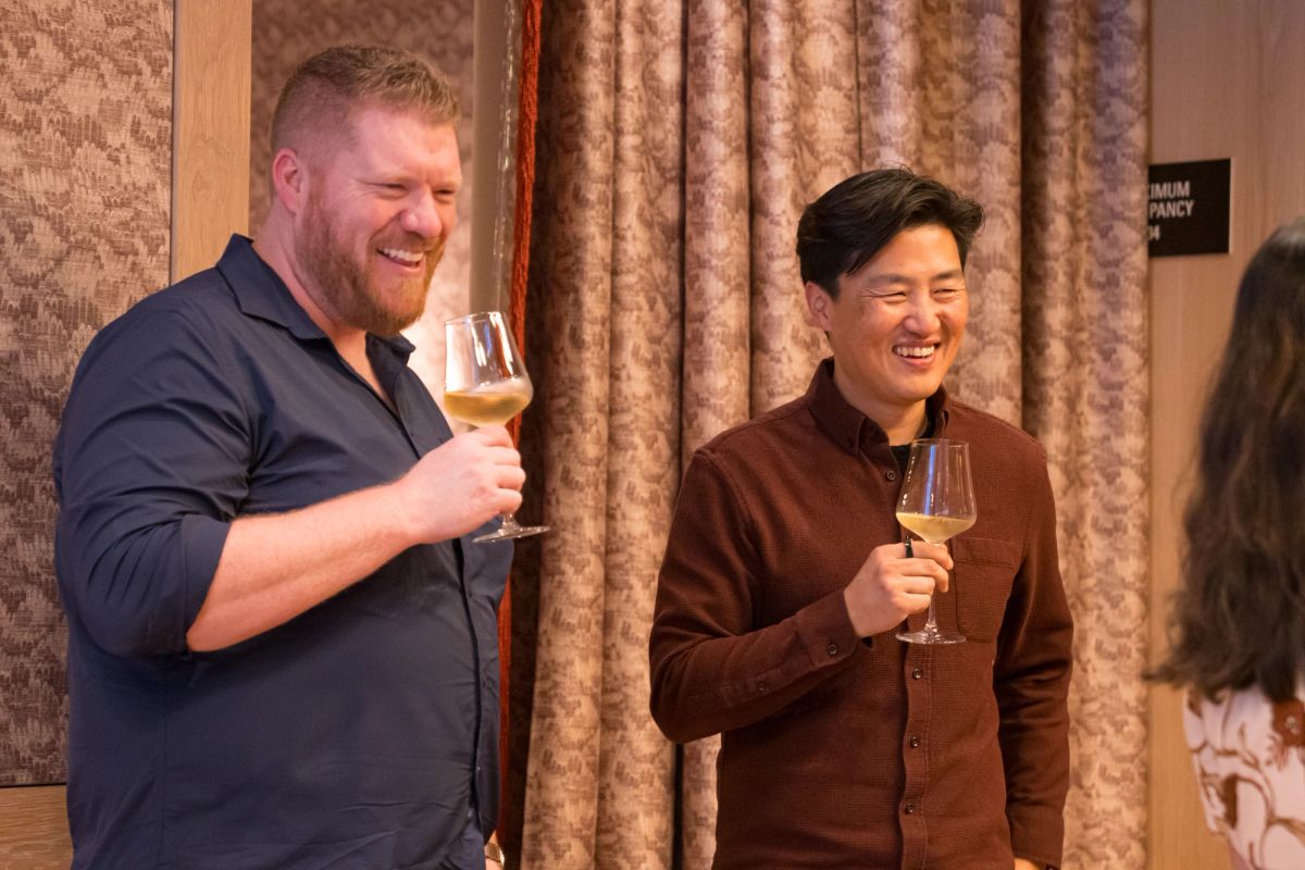 Two men in business attire raise wine glasses in a toast, smiling during an indoor event