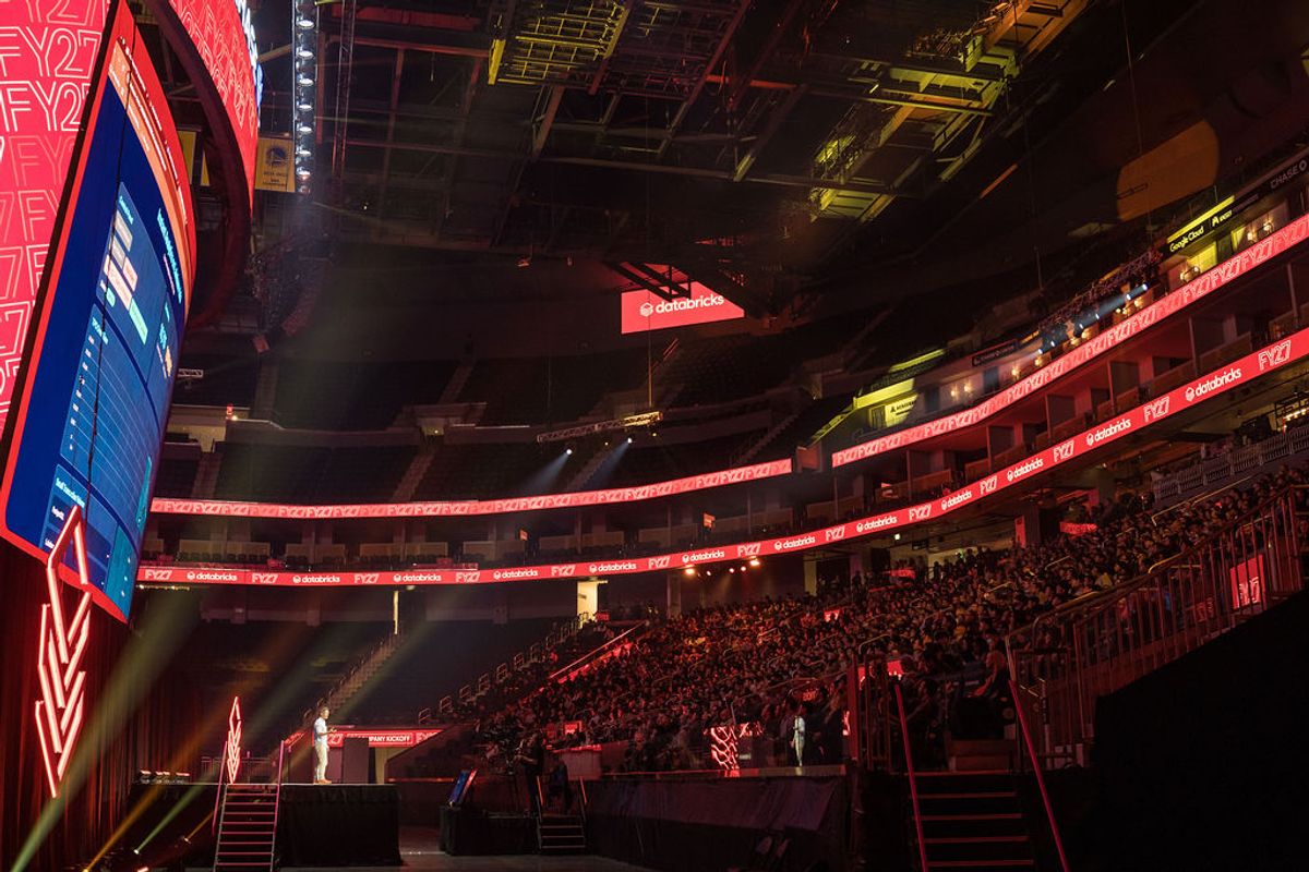 Large arena with red lighting, packed audience in tiered seating, and stage setup for conference event