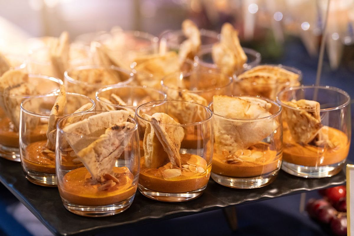 Clear glasses filled with orange dessert and decorative wafer cookies arranged on a tray at a reception