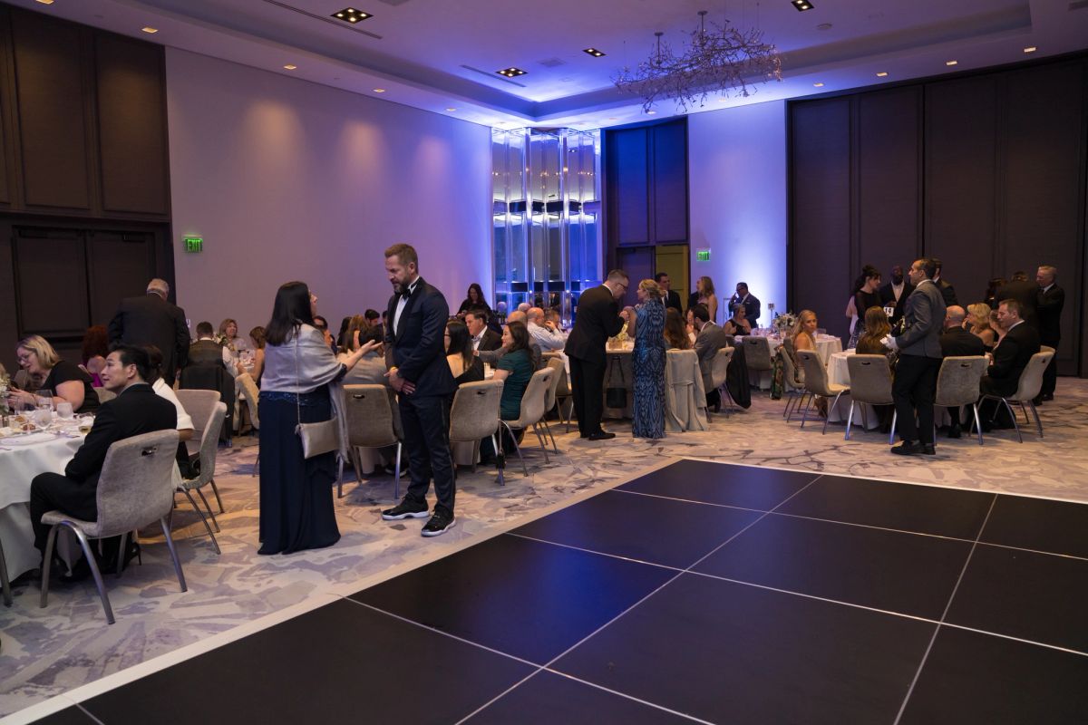 Formal gala event with guests in evening attire seated at round tables in an elegant ballroom with purple.