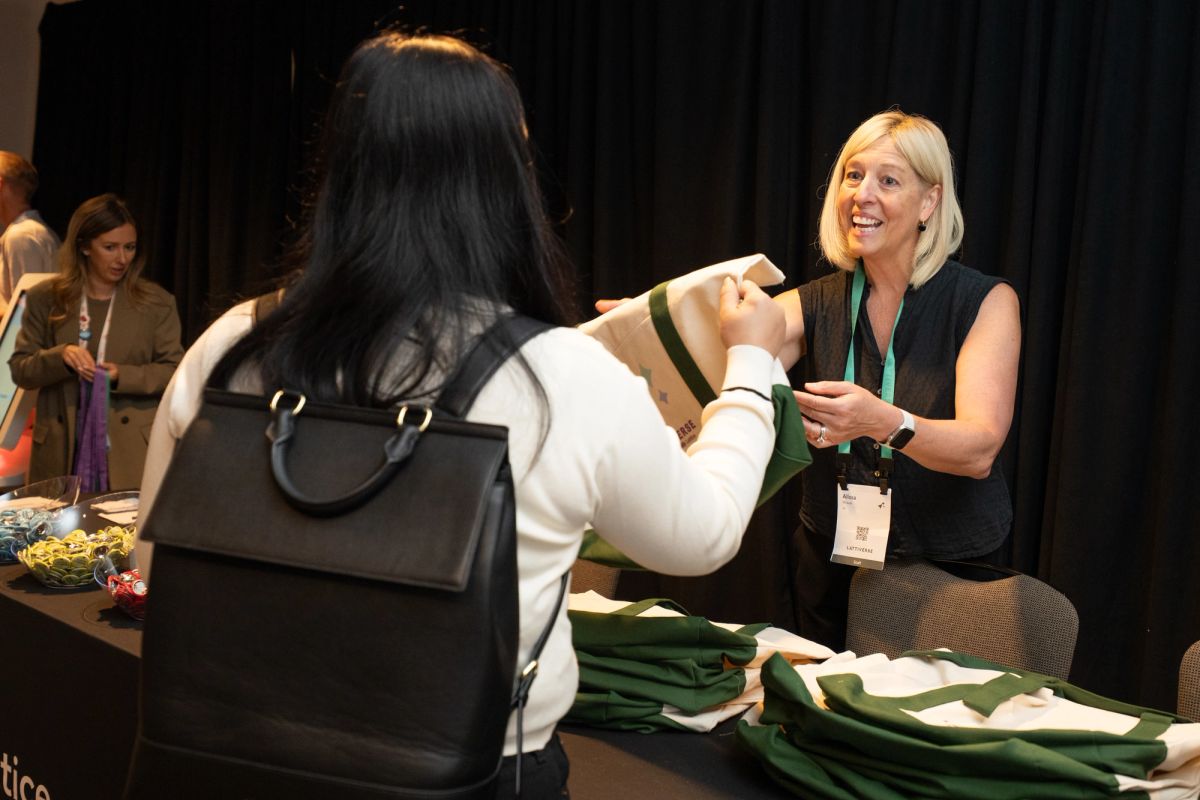 Attendee receives green branded merchandise from smiling staff member at conference registration table.