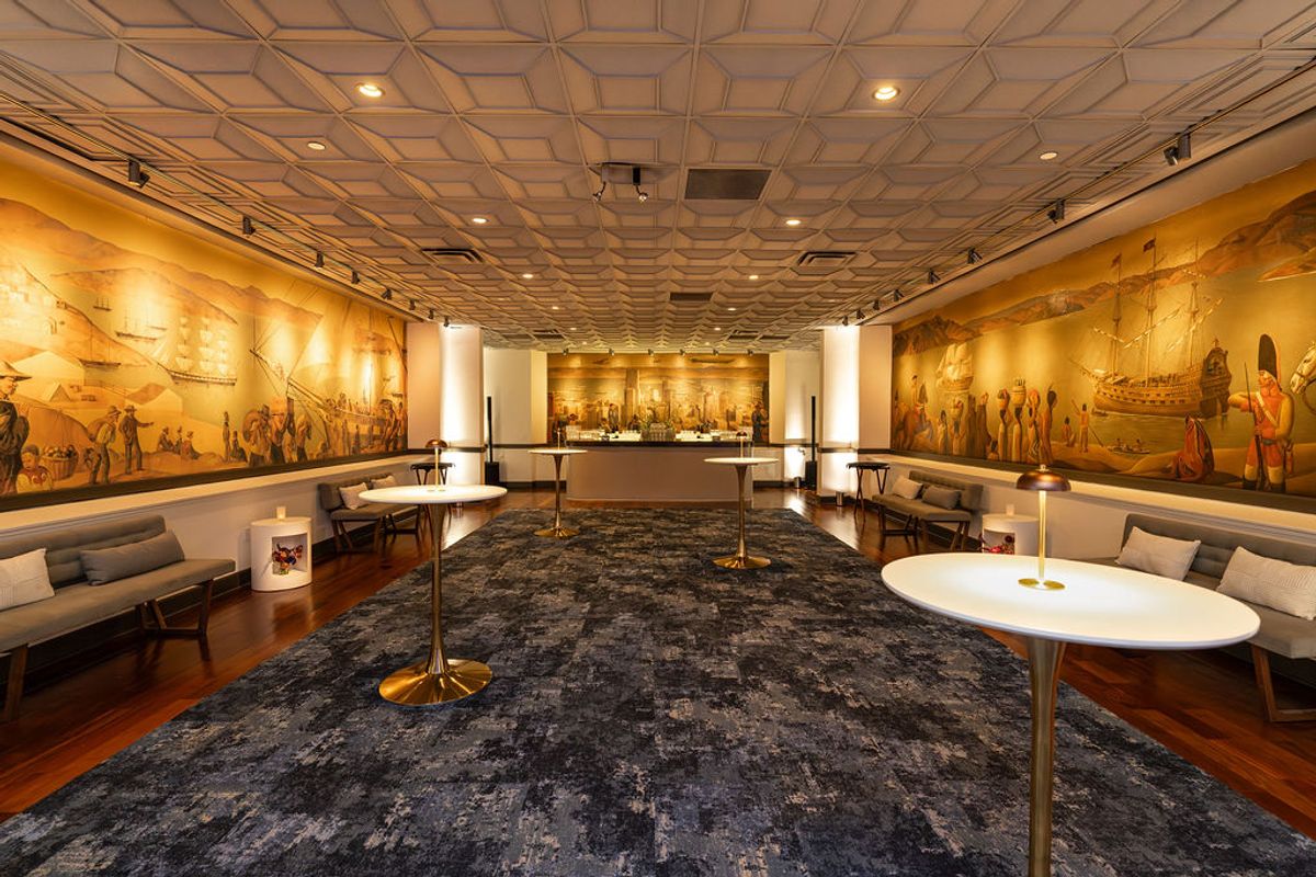 Elegant lounge with historical murals, white cocktail tables, gray seating, and geometric ceiling at.
