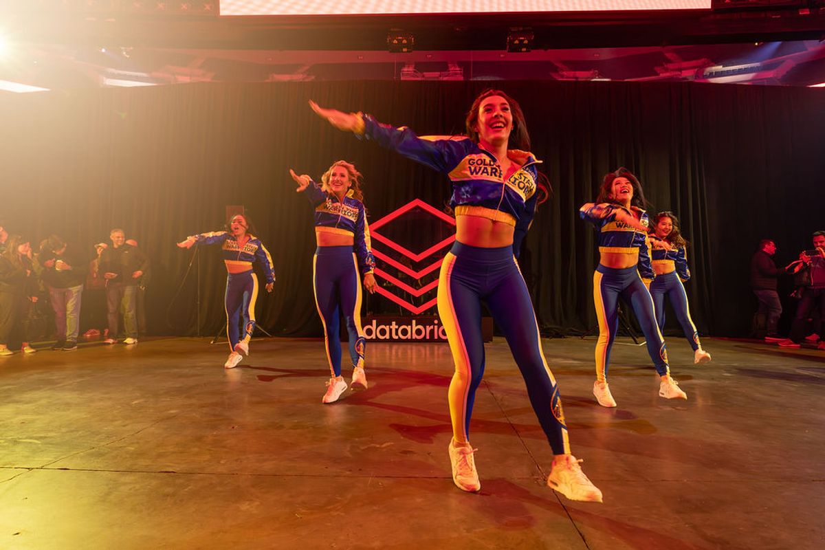 Cheerleaders in blue and orange uniforms perform on stage with Databricks logo backdrop at conference event
