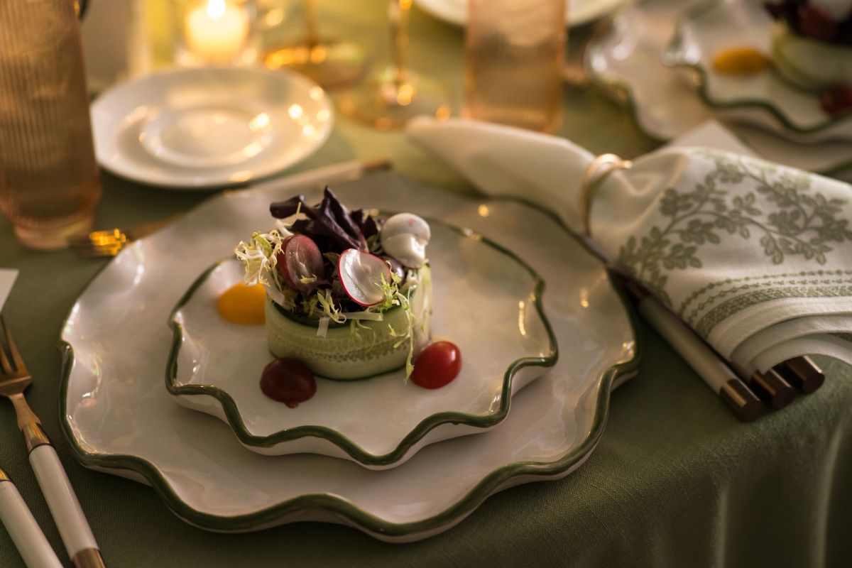 Elegant plated dessert with green mousse and garnishes on white scalloped plates at formal dining table