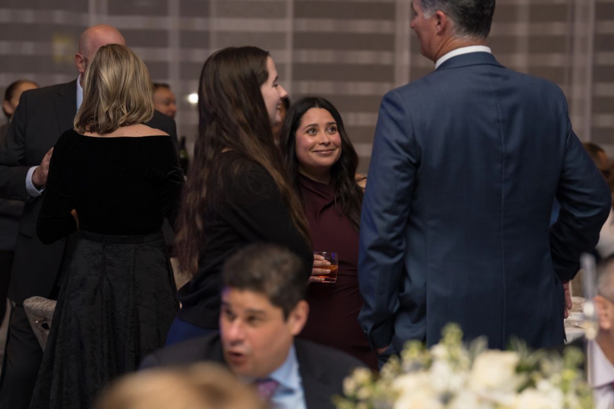 Attendees networking and socializing at formal evening event with men in suits and women in dress attire.