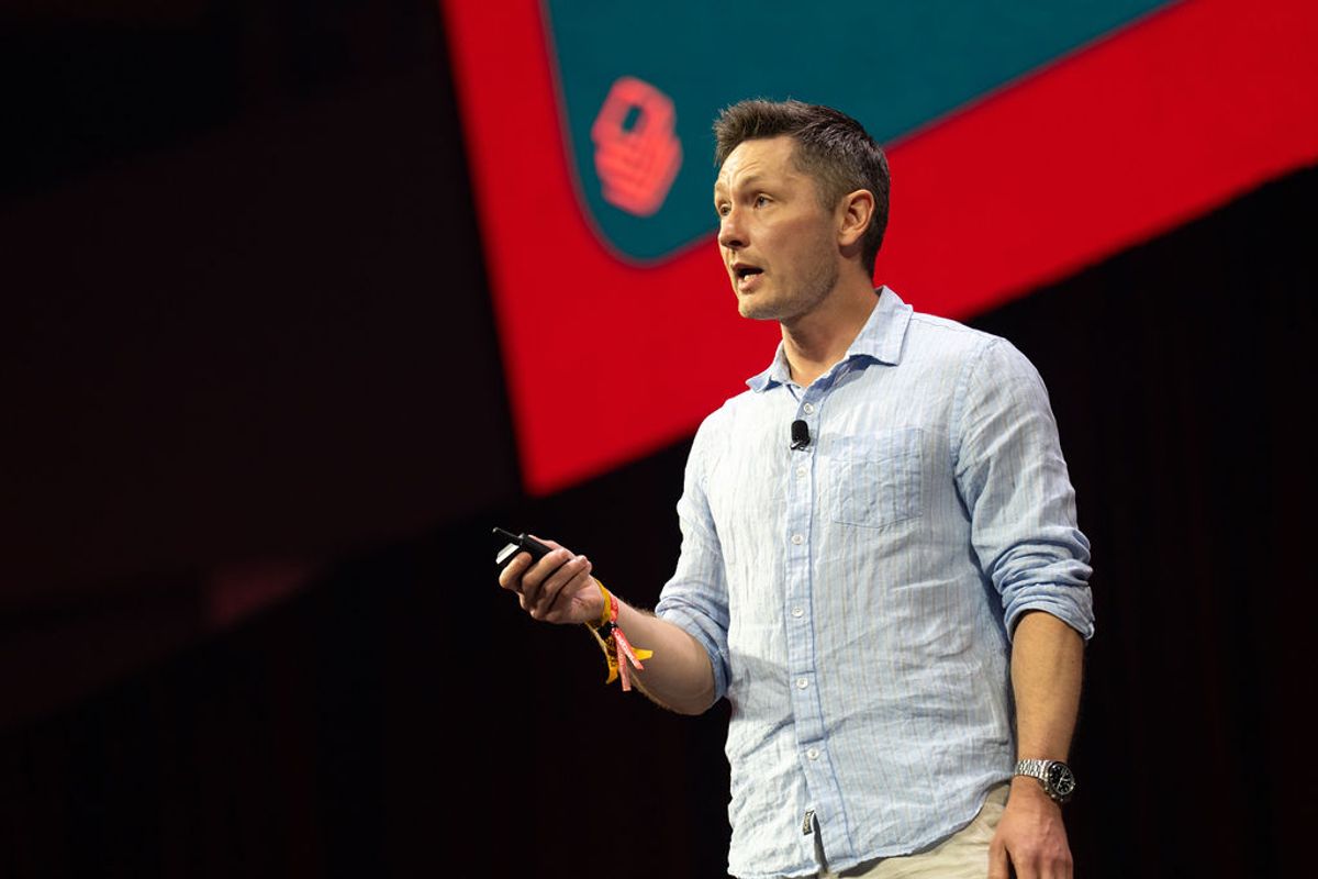 Speaker presenting on stage with microphone and mobile device at conference event