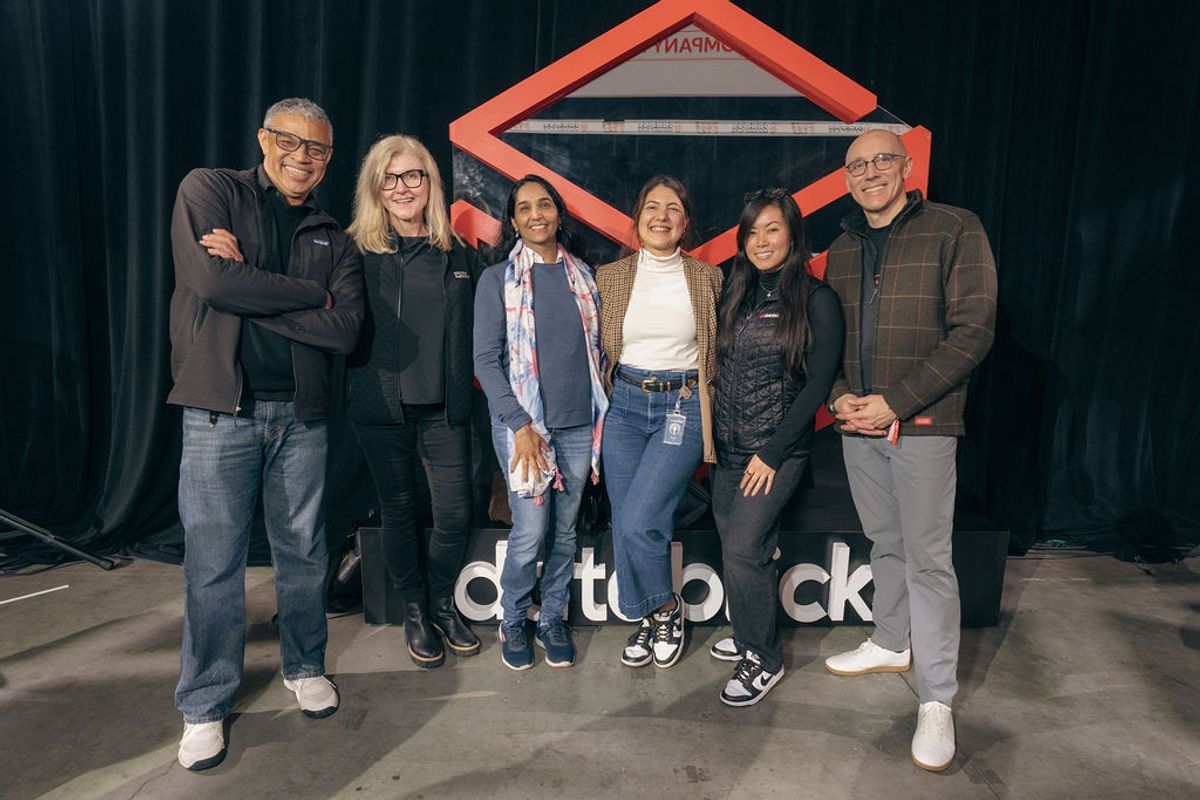 Six people posing together at a conference event with red geometric backdrop and "databrick" signage