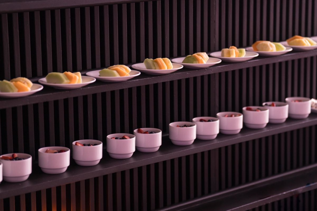 Two shelves displaying colorful desserts on plates and pink bowls against a dark slatted wall