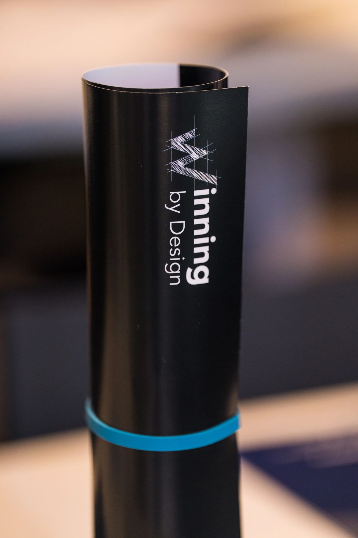 Black cylindrical award trophy with "ning by Design" text and geometric logo design at conference event
