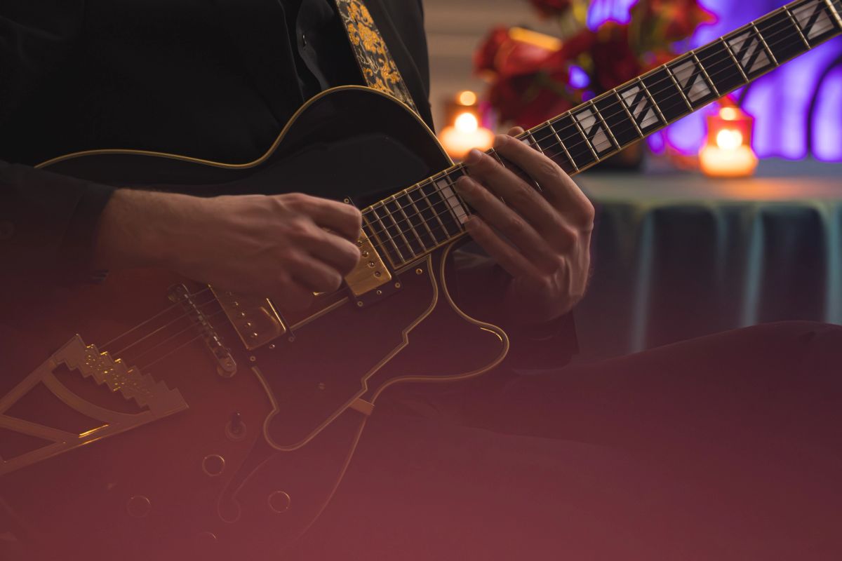 Musician playing black electric guitar on stage with warm stage lighting and blurred background