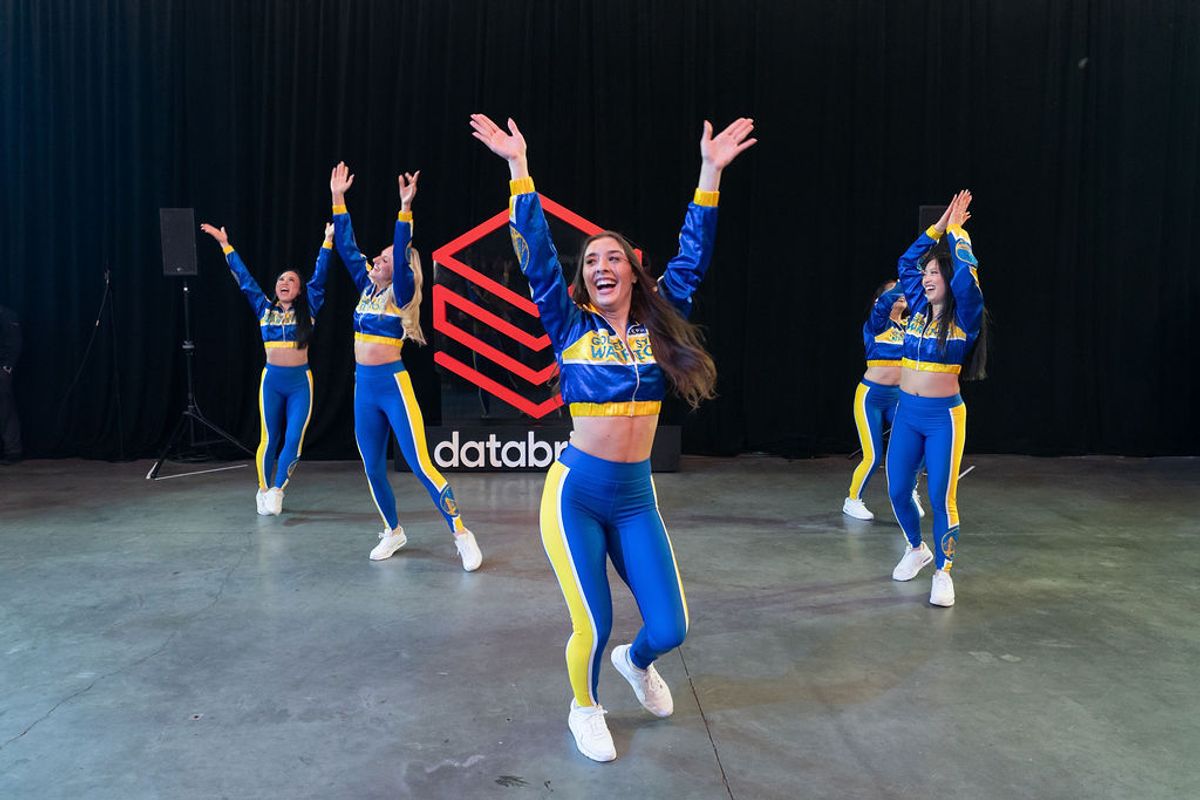 Cheerleaders in blue and yellow uniforms performing with arms raised on stage at conference event