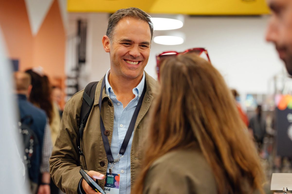 Two conference attendees having a conversation in a busy event venue with colorful decor and lighting