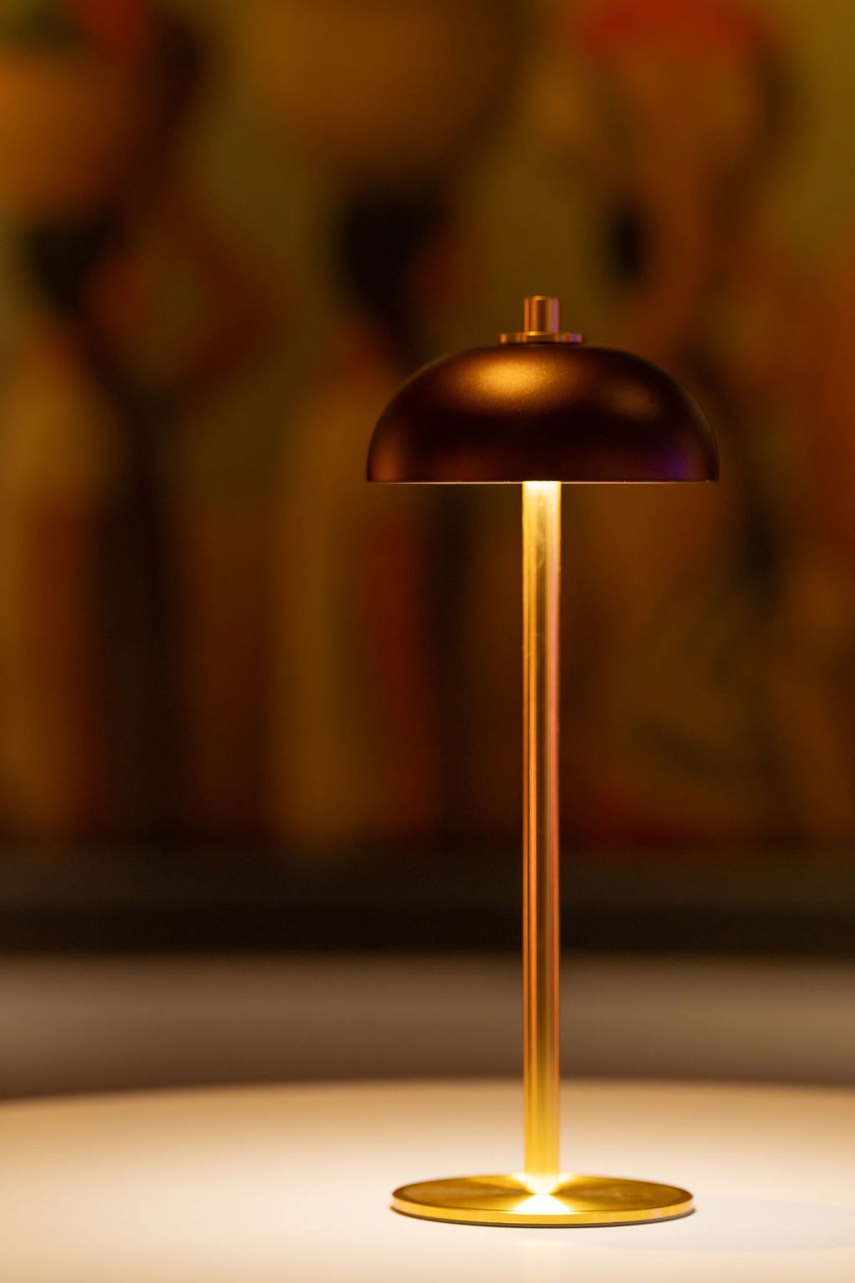 Modern copper table lamp with dome shade glowing warmly against blurred warm-toned background