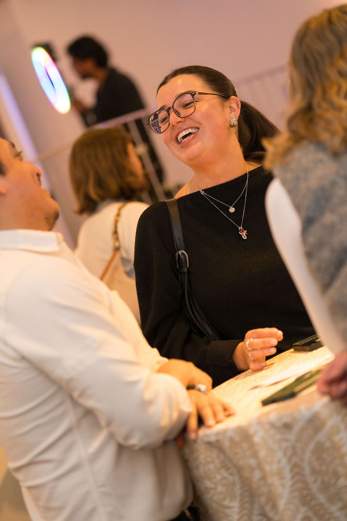 Woman in black top and glasses laughs while talking with other attendees at networking reception
