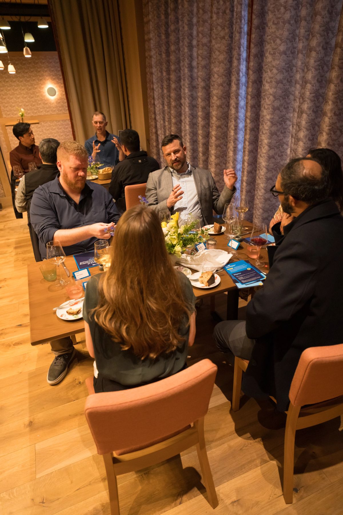 Business professionals seated around table in animated discussion at networking event in modern restaurant.