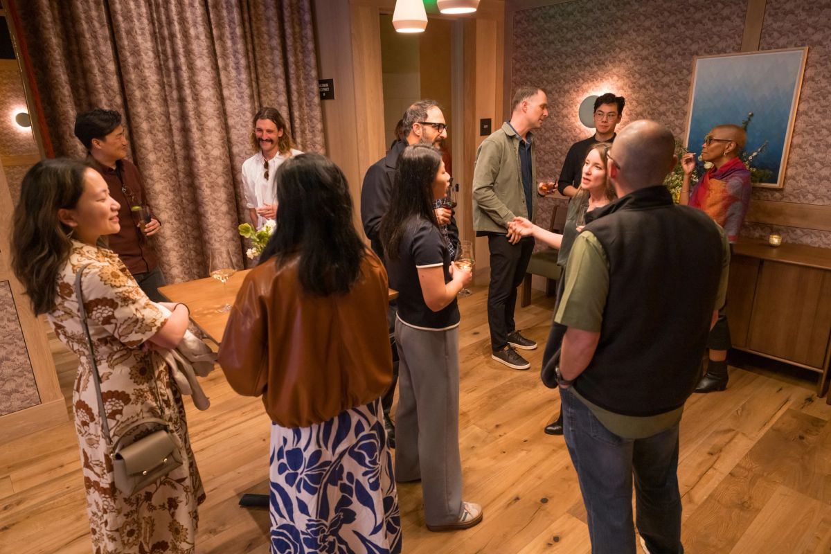Attendees networking and conversing in small groups during a panel discussion event in a wood-floored room.