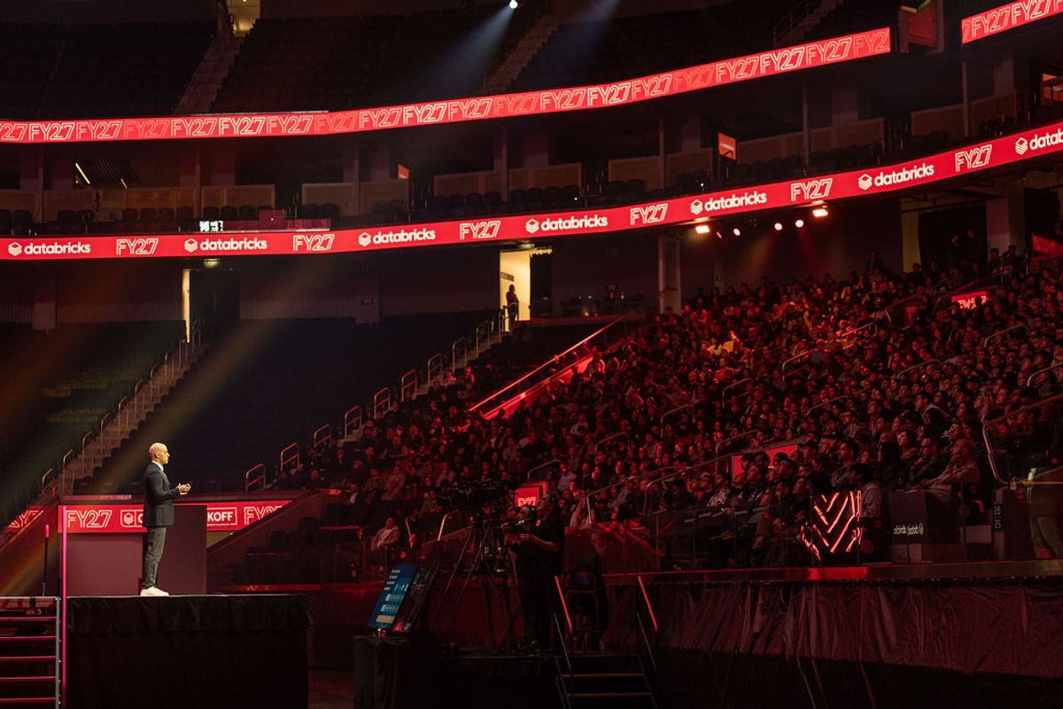 Speaker at podium addressing packed auditorium with red lighting and FYZ7 branding on digital displays